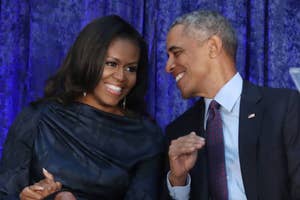 Michelle and Barack Obama sitting together, smiling, Barack gesturing with his hand. Michelle wears a draped top
