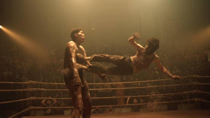 Escena de lucha con dos personajes en el aire dentro de un ring ante una multitud