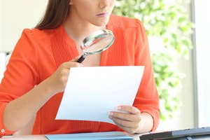 Woman examining document with magnifying glass, symbolizing financial scrutiny