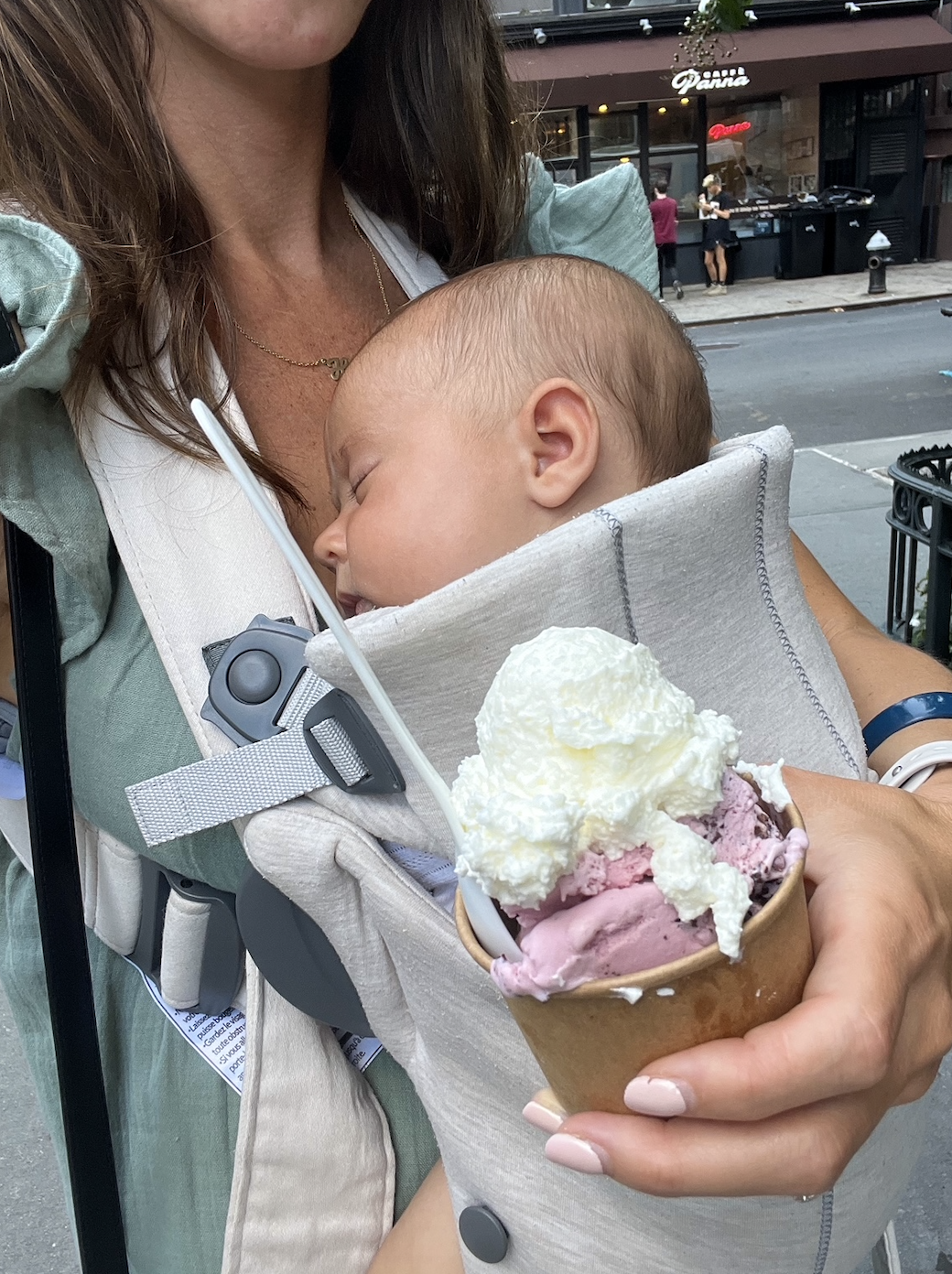 Woman holding a sleeping baby in a carrier, with an ice cream cone in her hand