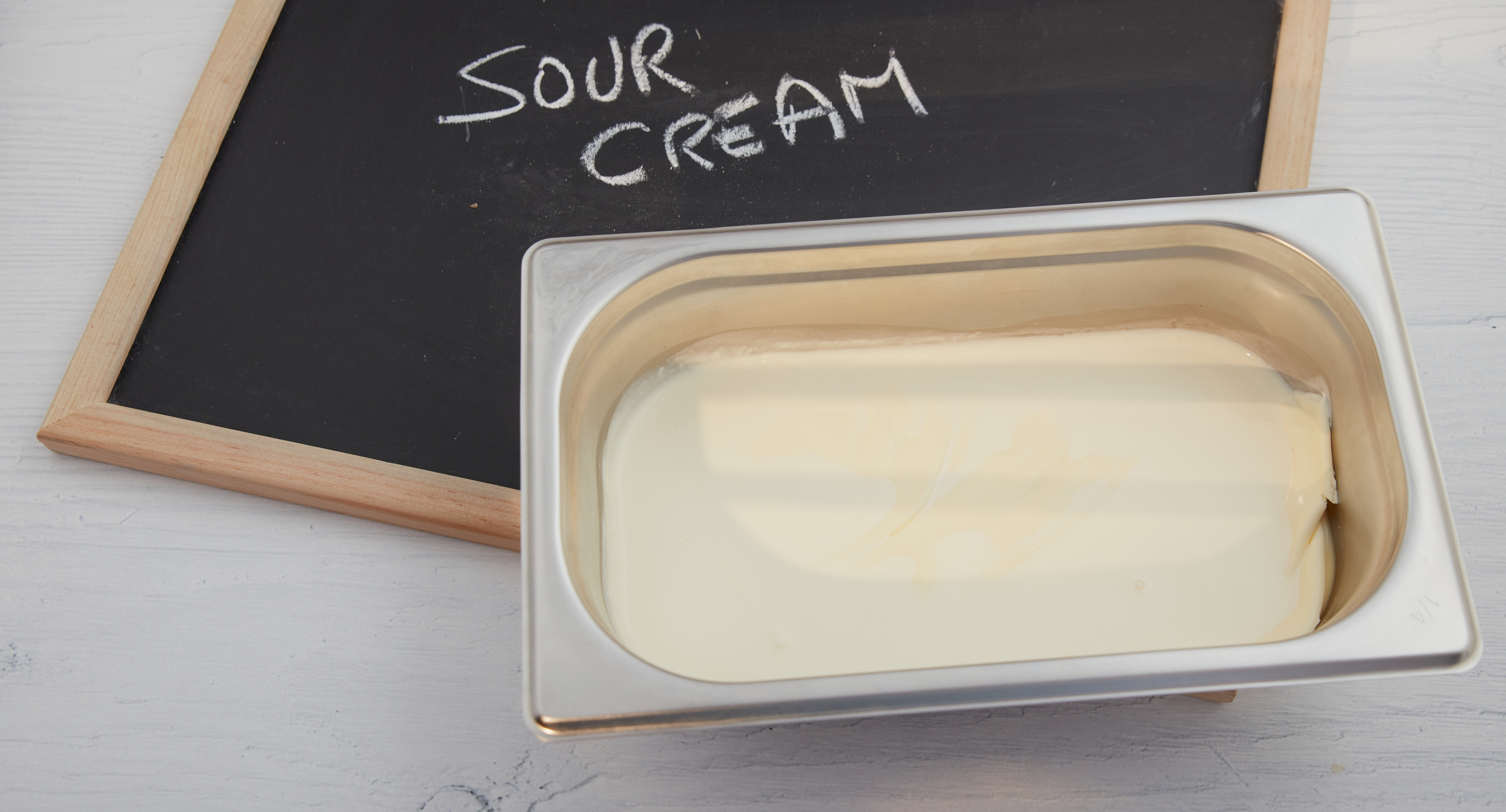 A block of butter in a dish beside a chalkboard with 'SOUR CREAM' written on it