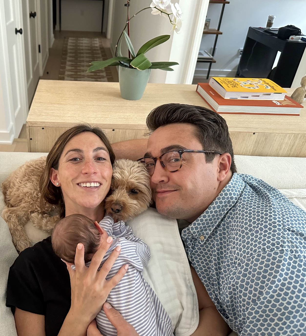 Family portrait with two adults, a baby, and a dog, lounging together and smiling