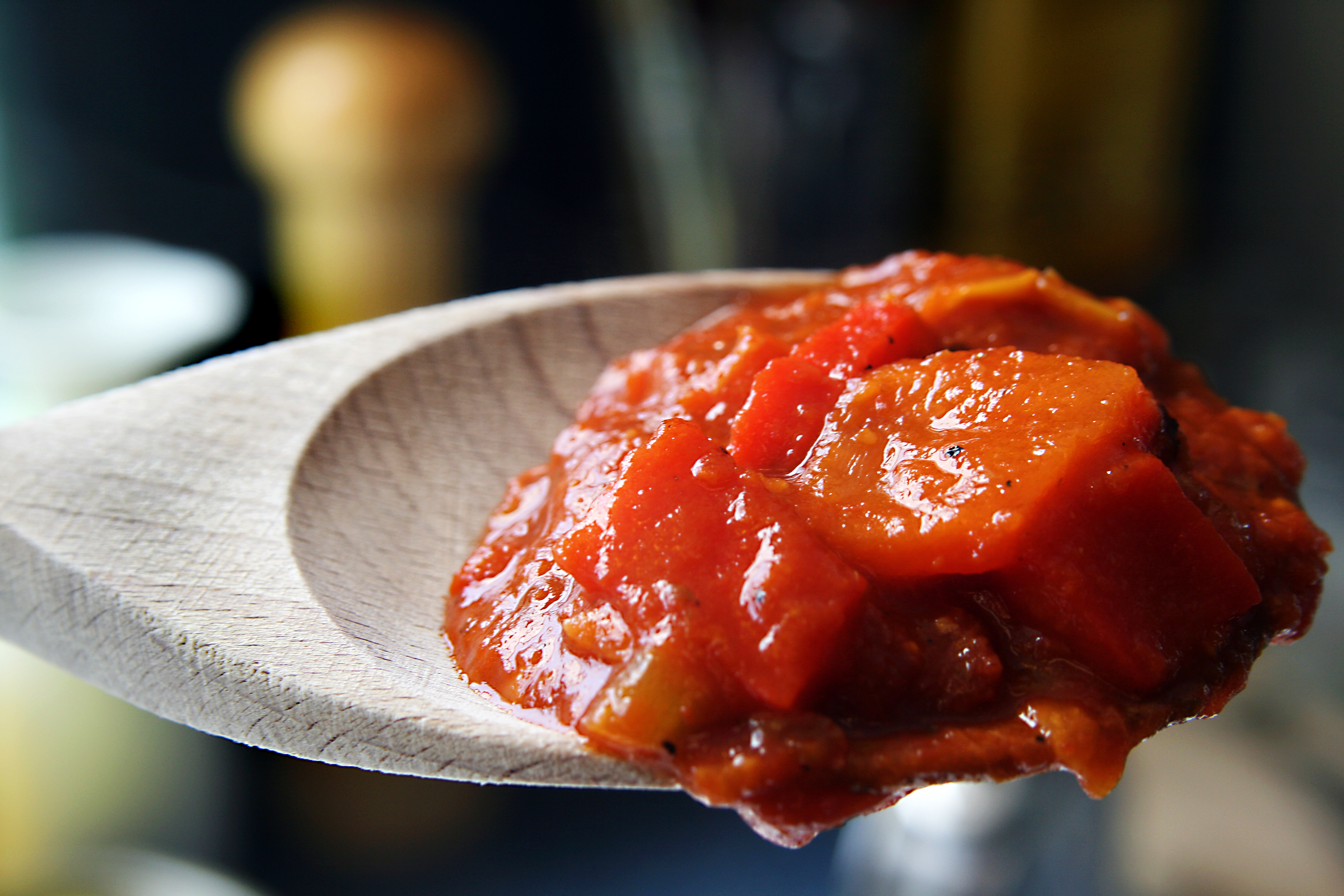 A close-up of a wooden spoon holding a chunky tomato sauce