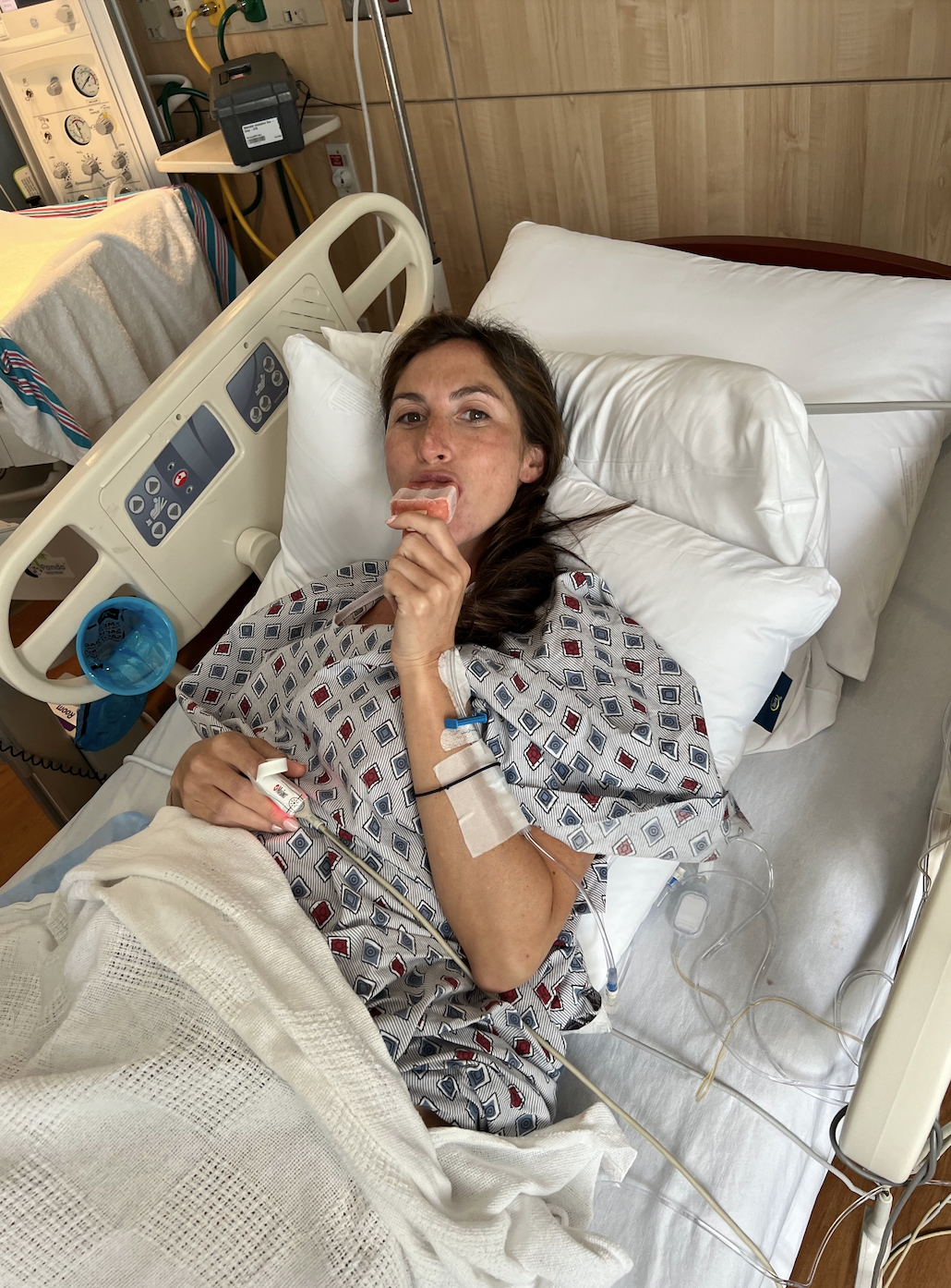Person in hospital bed with IV, holding something in mouth