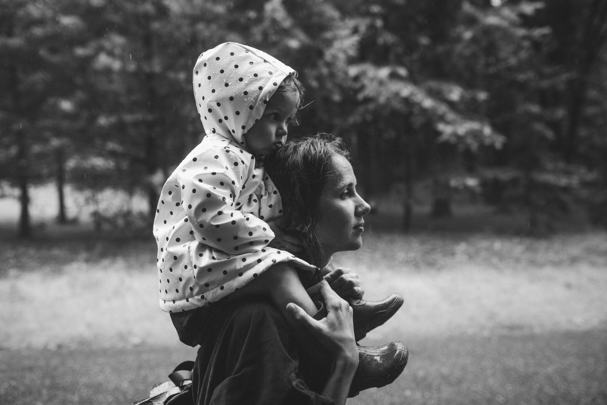 Child in a hooded polka-dot top sits on an adult&#x27;s shoulders, both looking away contemplatively