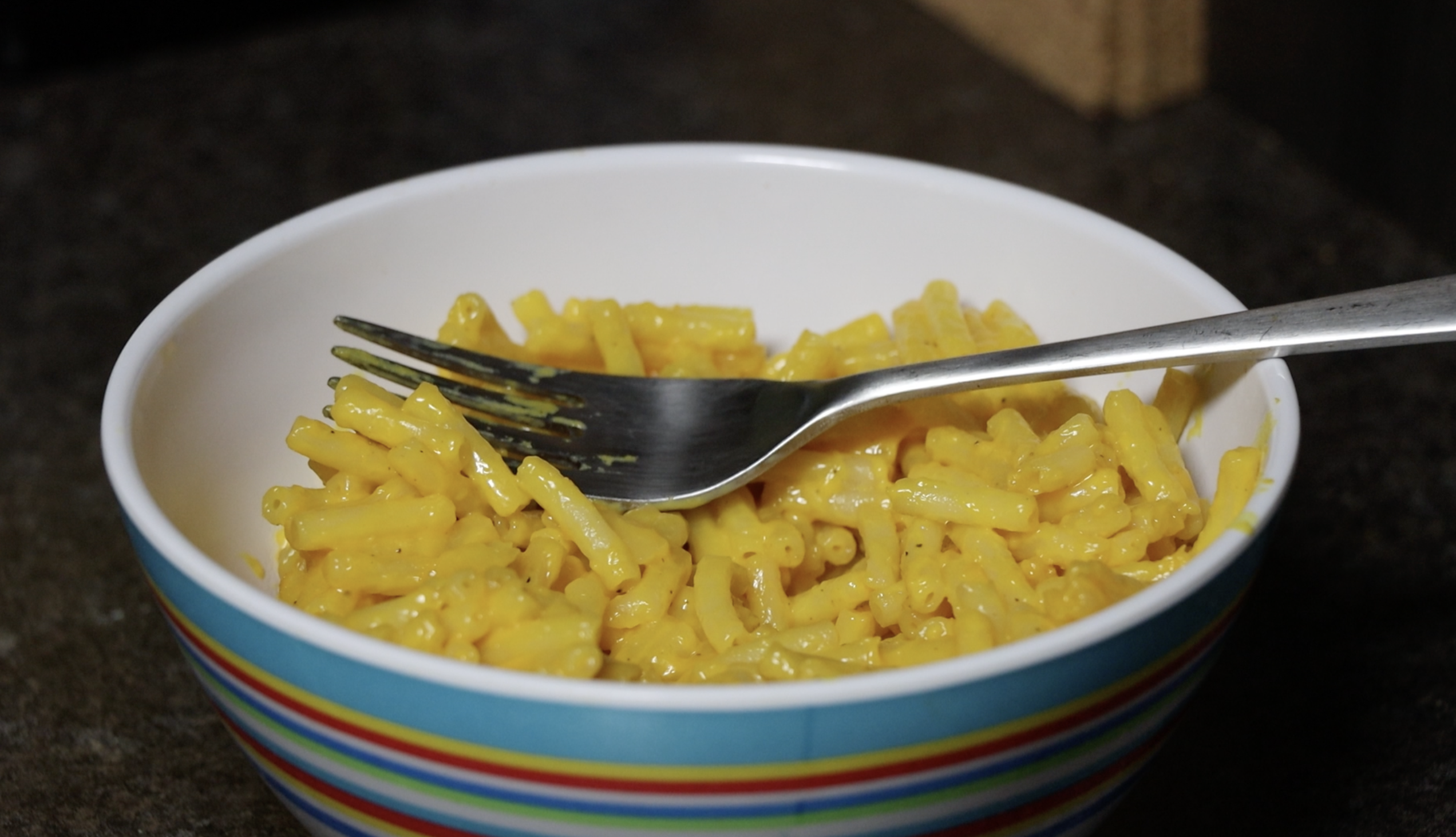 Bowl of macaroni and cheese with a fork on a kitchen counter