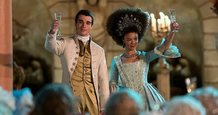 Personajes de época brindando en una fiesta, la mujer luce un vestido estilo siglo XVIII y el hombre un traje con chaleco