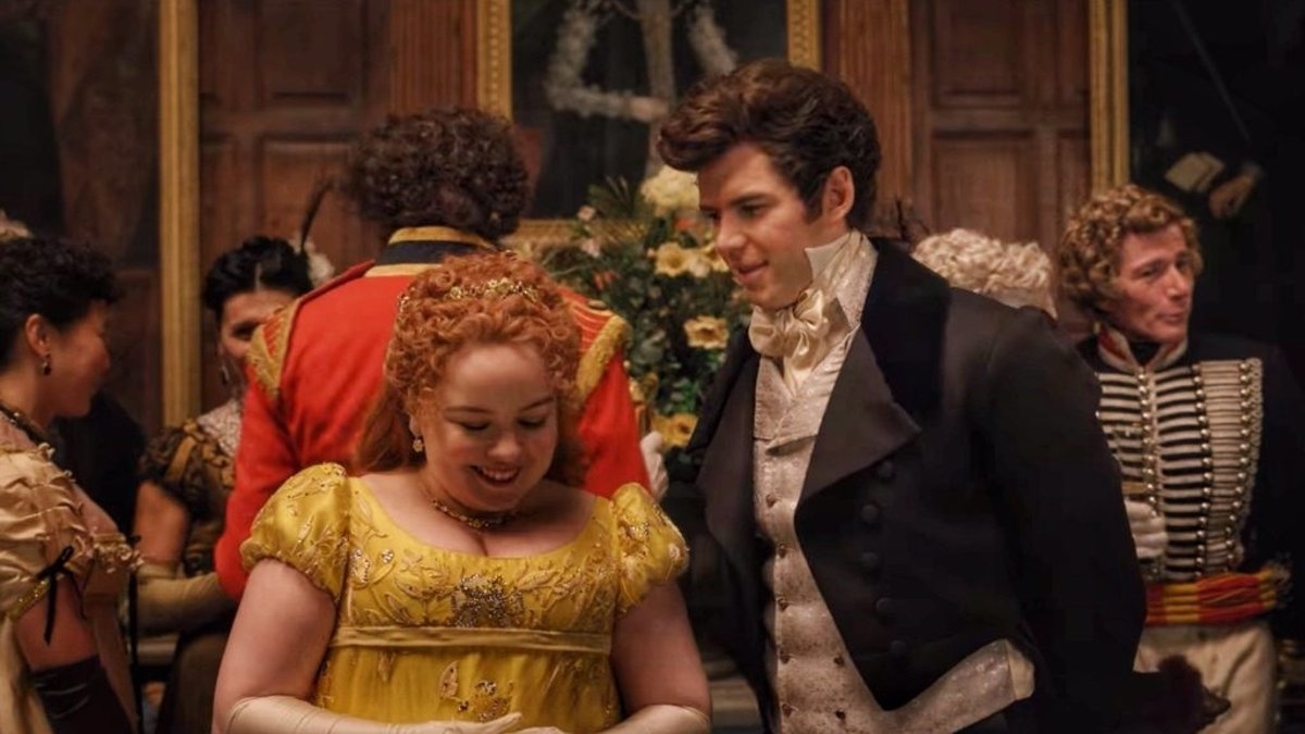 Personajes de la serie "Bridgerton" en trajes de época en un baile, hombre y mujer sonriendo y conversando