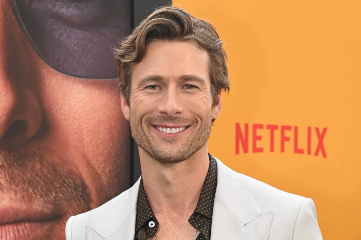 Man in a patterned shirt smiling at a Netflix event, standing in front of a promotional poster