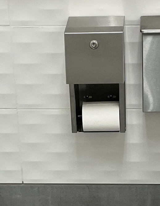 Dispenser with an upside-down toilet paper roll against a tiled wall