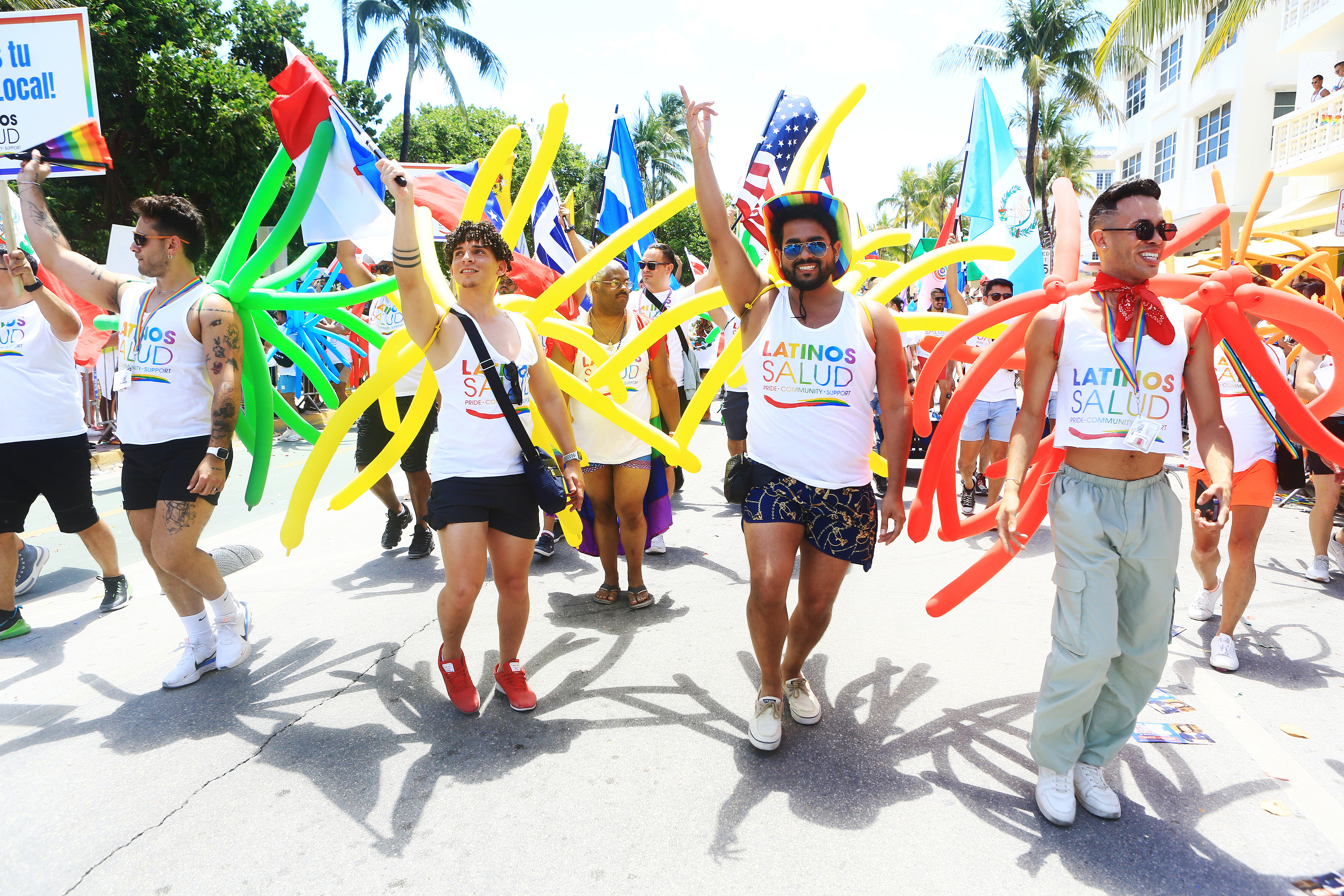 Group of people marching with "Latinos Salud" shirts and carrying colorful ribbons during a pride parade
