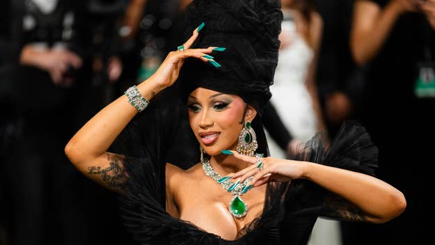 Cardi B in an extravagant black outfit with a large headpiece and statement jewelry at an event