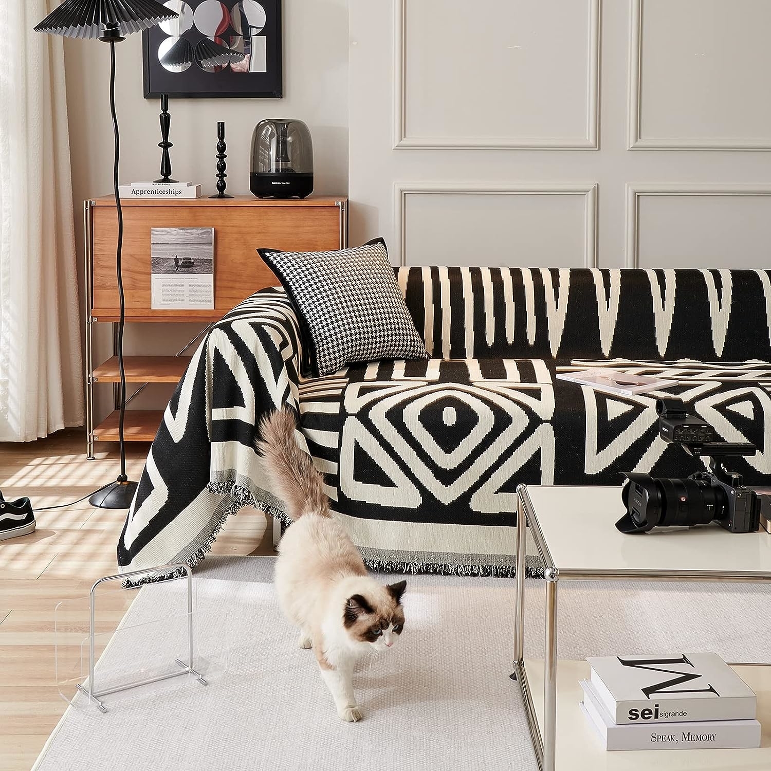 A cat walks by a stylish sofa draped with a patterned blanket, in a chic living room setting