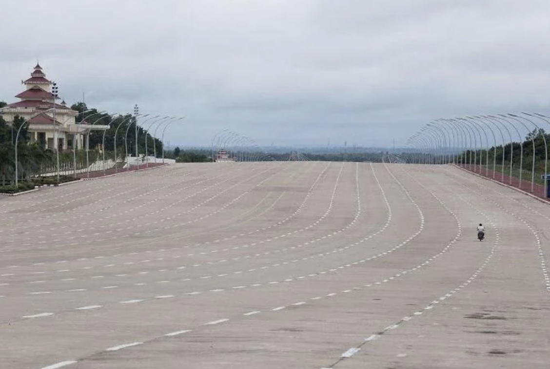 Wide empty boulevard with a large building in the distance and two people walking