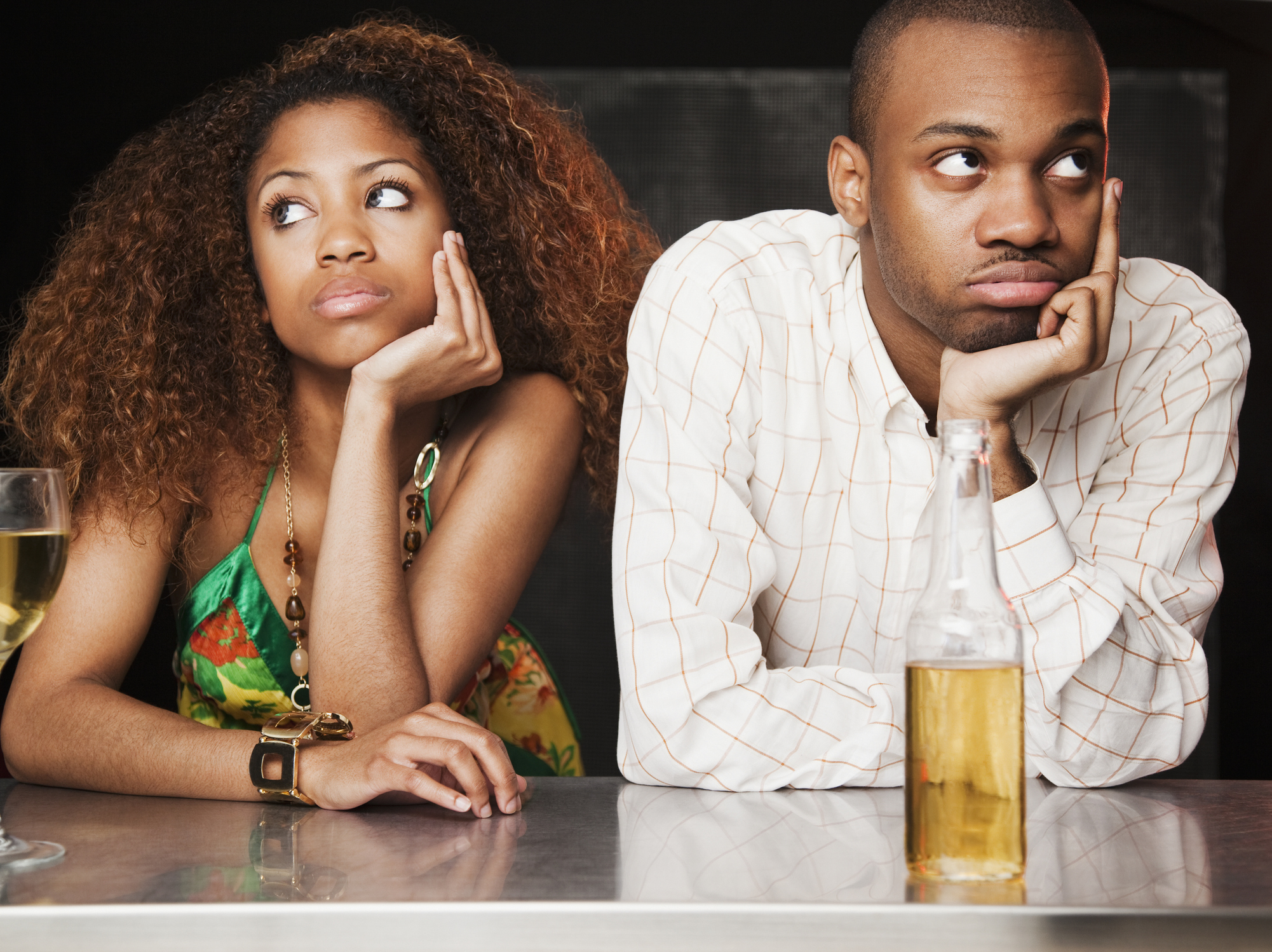 Two people sitting at a bar appear disinterested in each other, both looking away with bored expressions