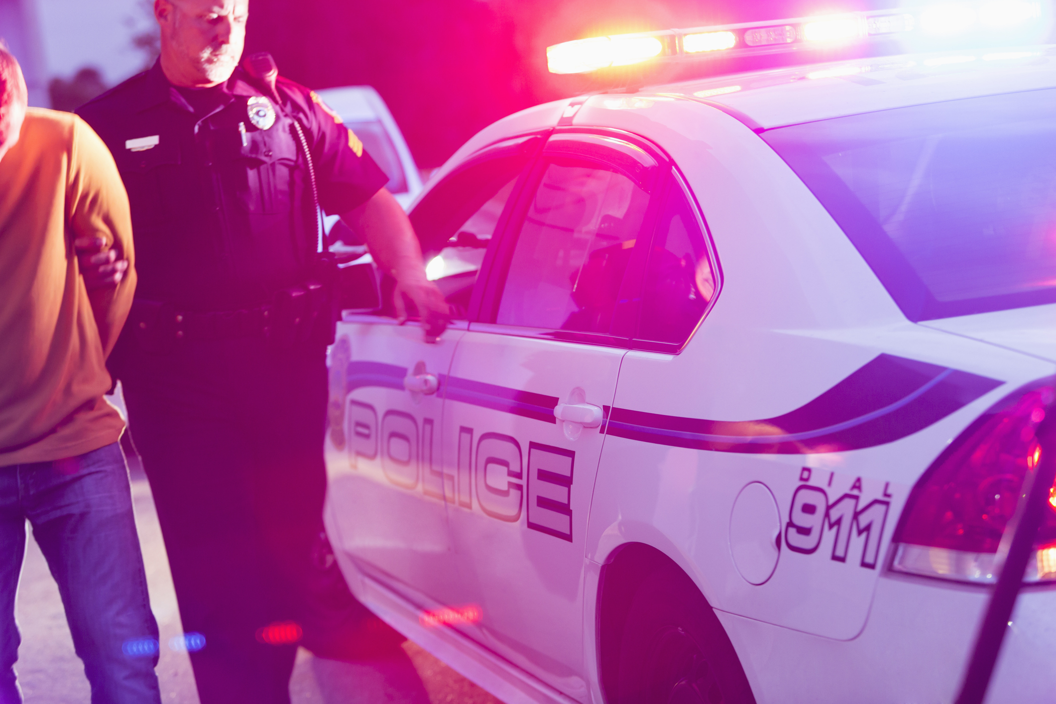 A police officer standing next to a patrol car speaks with an individual during dusk