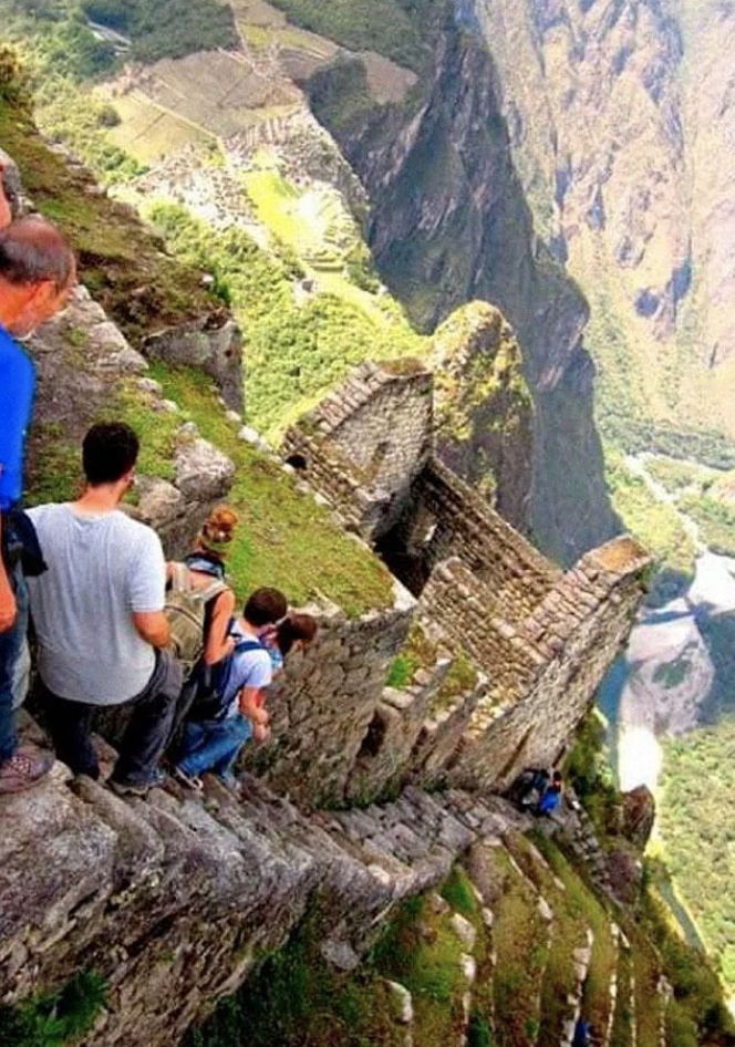 Tourists on steep stairs at Machu Picchu overlooking ancient ruins and landscape