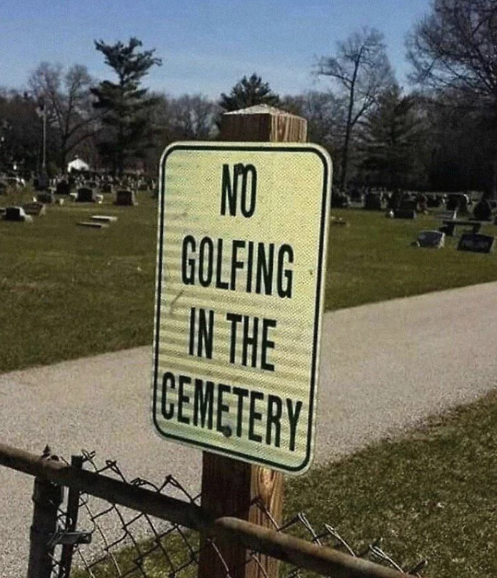 Sign reads &quot;NO GOLFING IN THE CEMETERY&quot; beside a fence with a graveyard in the background