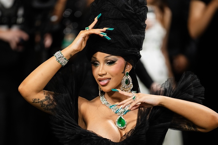 Person at a music event in a plumed hat and jewel-adorned outfit, posing for cameras