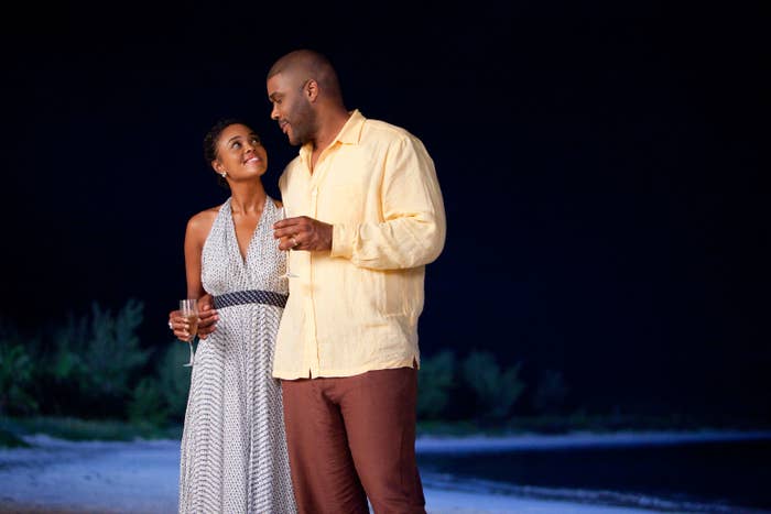 Sharon Leal and Tyler Perry standing close on a beach at night, one holding a wine glass. They are engaging in a conversation