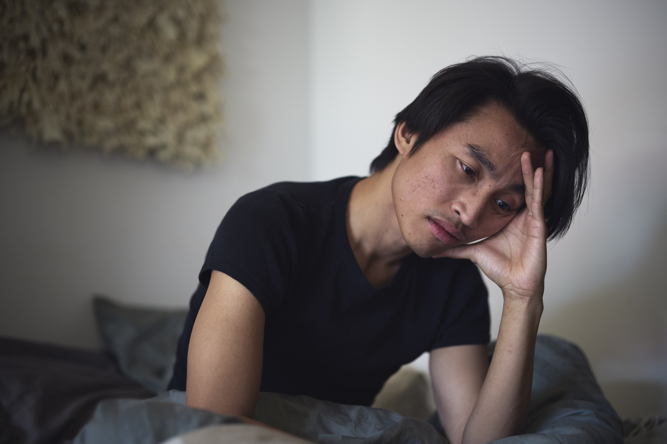 Person looking tired while resting head on hand, sitting on a bed, possibly stressed or contemplating work-related issues