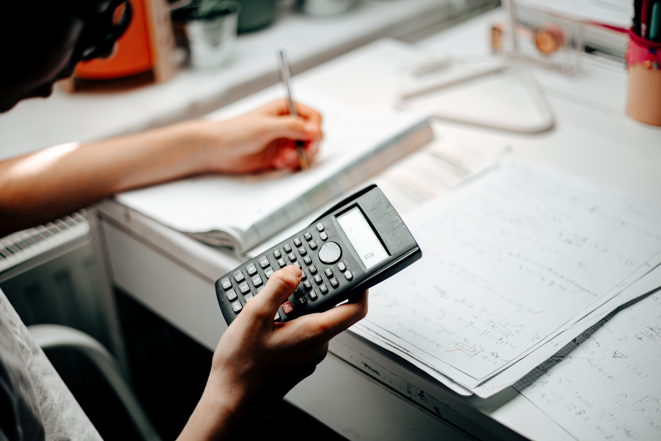 Person at a desk using a calculator with papers and a laptop nearby