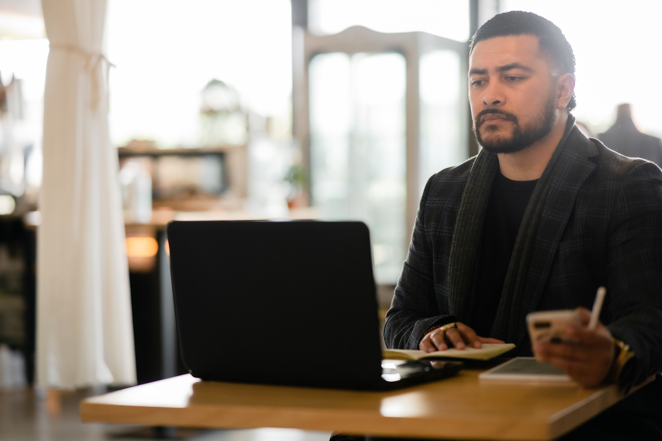 Man in business attire focused on work at laptop, with smartphone in hand, at office desk