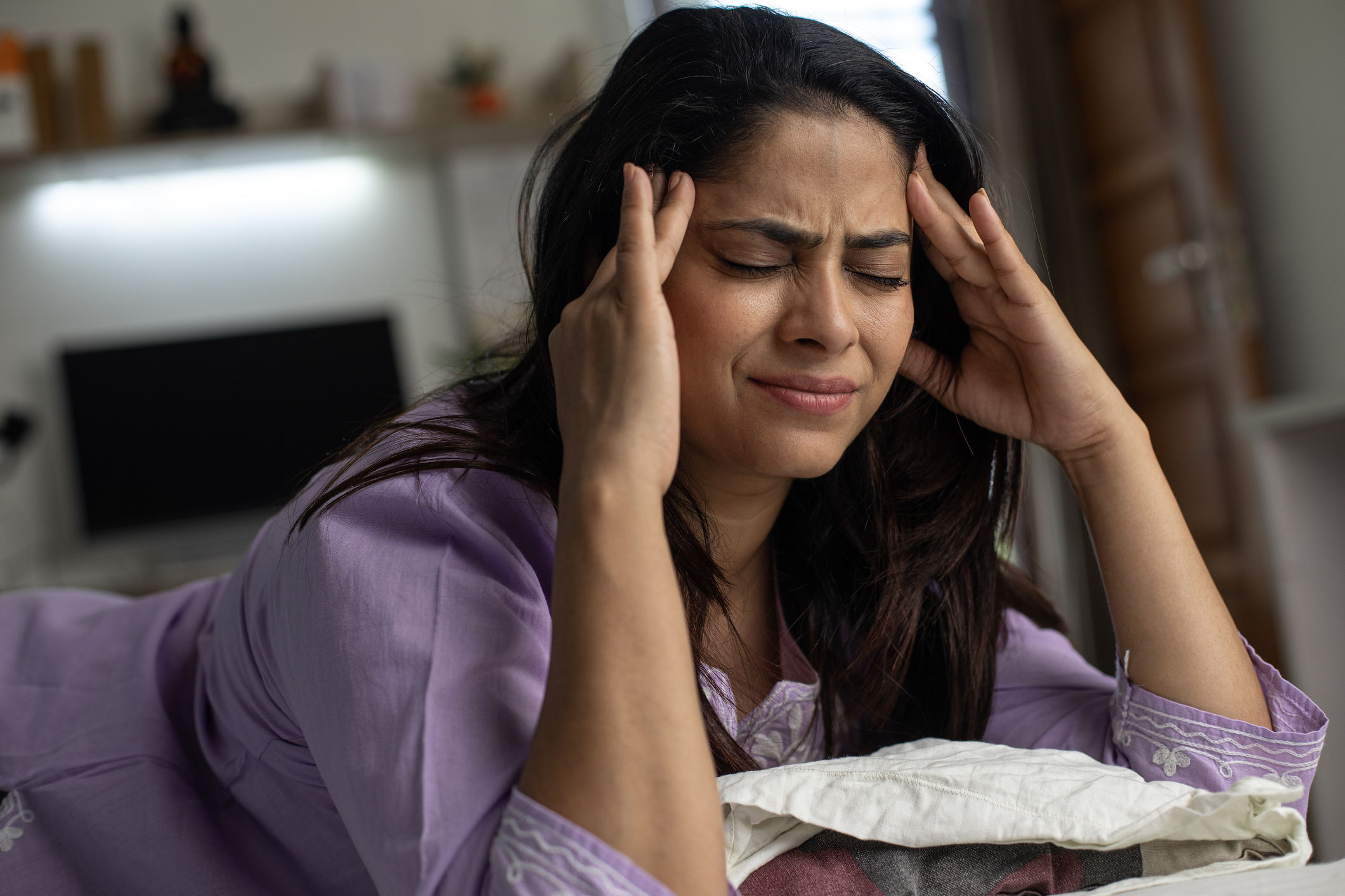 Woman appears stressed, resting her head in her hands, sitting by a table with paperwork