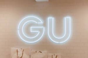 GUロゴのネオンサイン、白壁に取り付けられ、下にGUのショッピングバッグが並んでいる。
