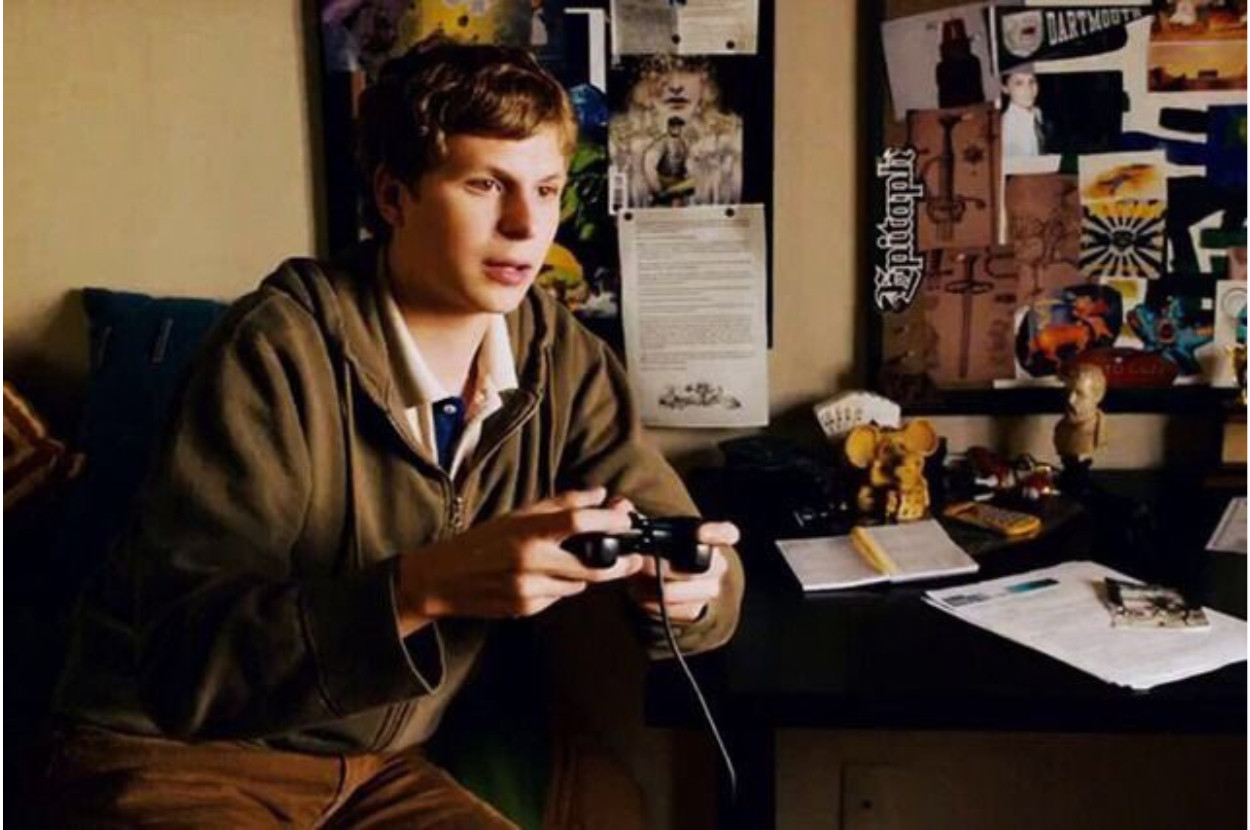 A person holding a game controller with focus and intensity, surrounded by posters and clutter typical of a gamer's room