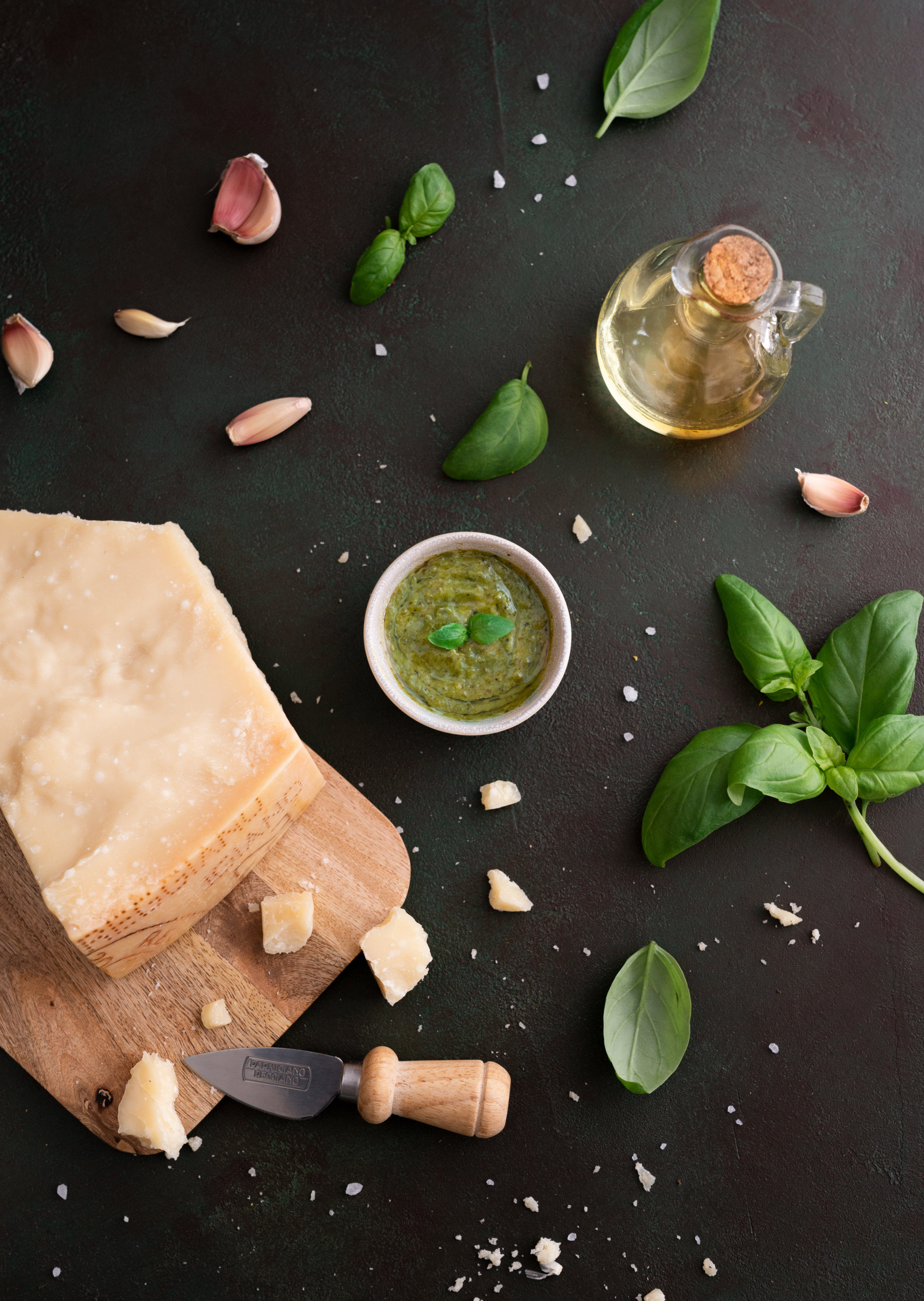 Ingredients for Italian cuisine with cheese, garlic, basil, and olive oil on dark surface