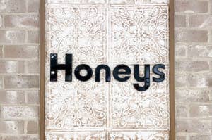 レンガ壁に取り付けられた装飾的なパネルのドアに「Honeys」と書かれたサインがあります。