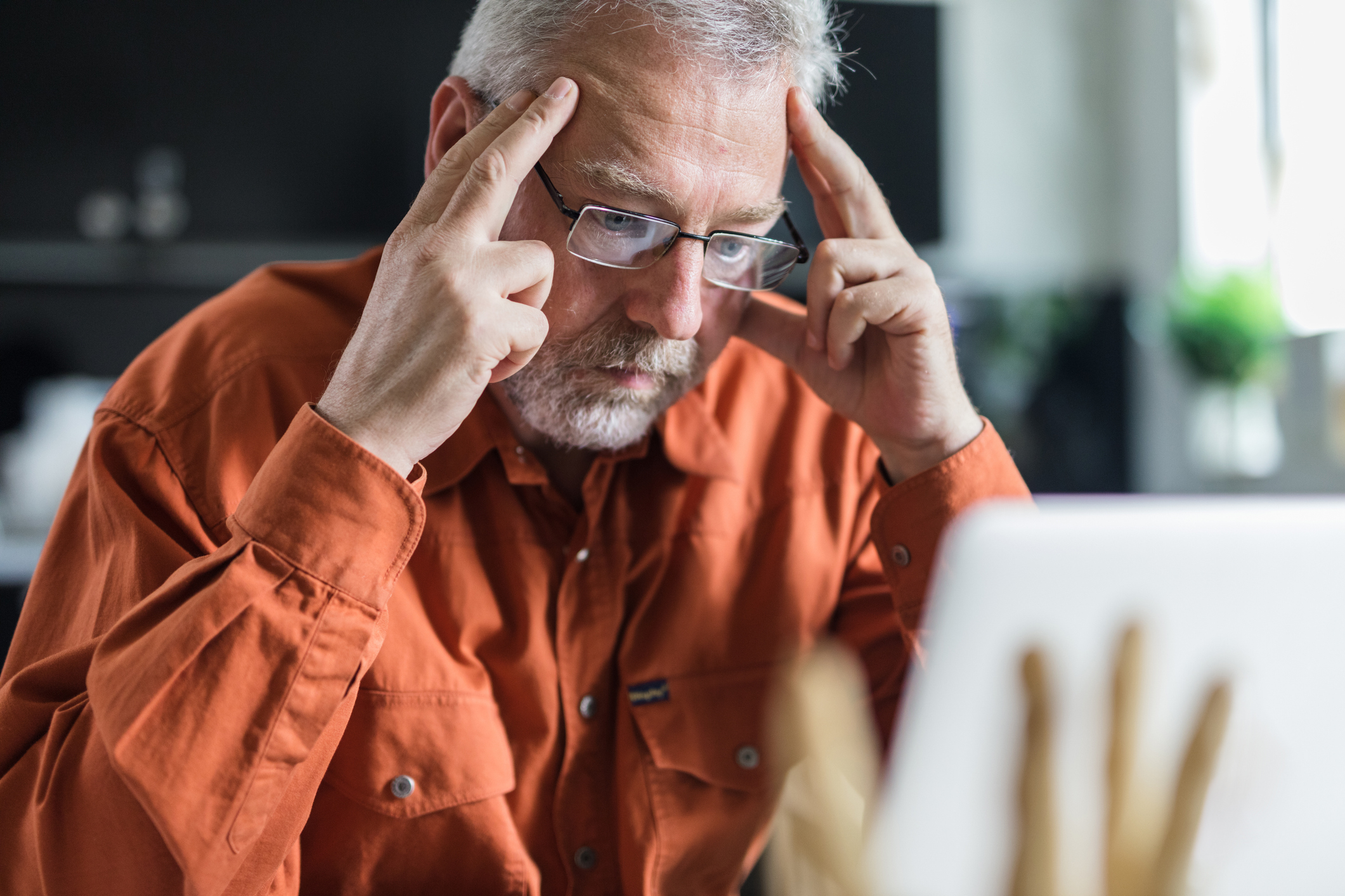 Man in glasses concentrating on screen, hands on temples, showing effort or concern