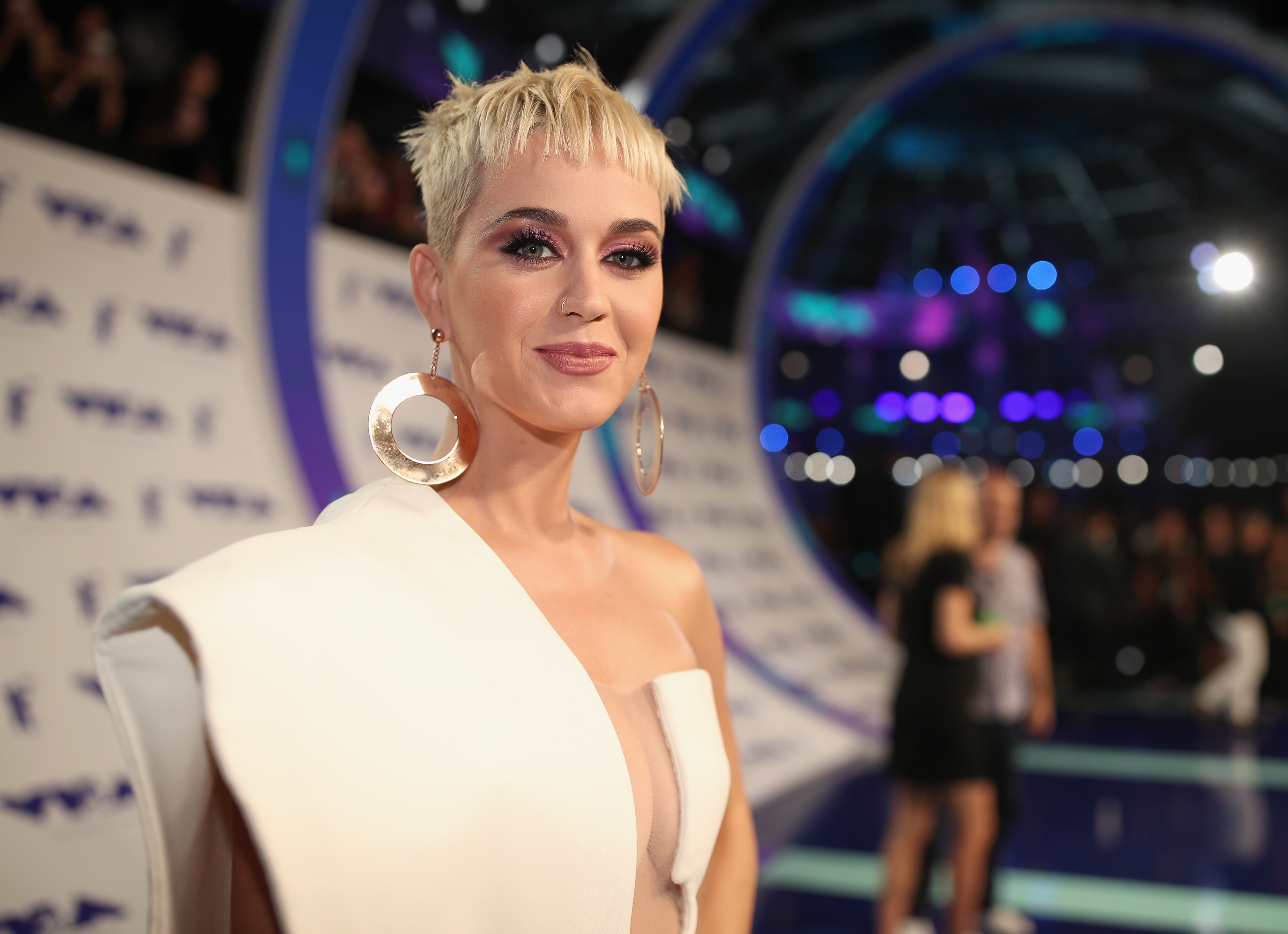 Katy Perry in a chic asymmetric white outfit with large hoop earrings at an event