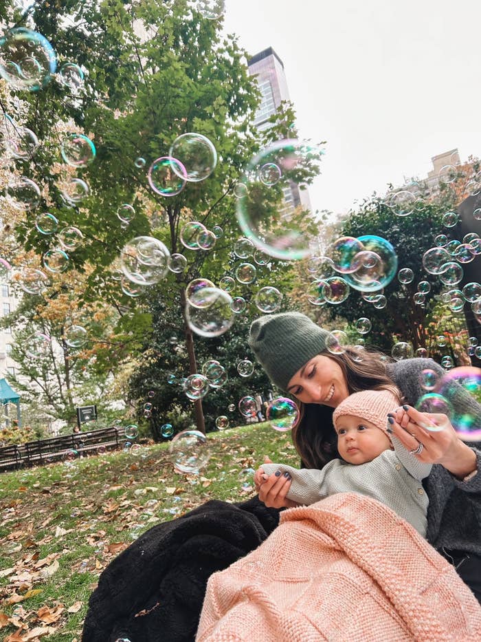 Woman and baby sitting on a blanket outdoors surrounded by floating soap bubbles