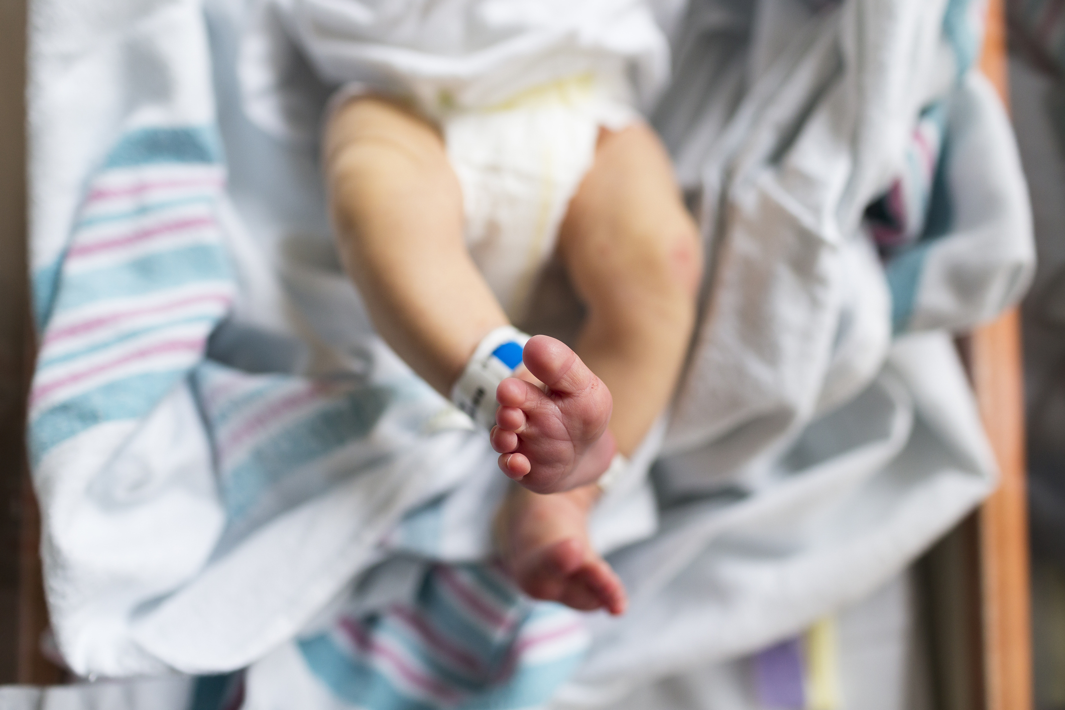 Newborn baby with hospital ID band holding an adult&#x27;s finger, wrapped in a striped blanket