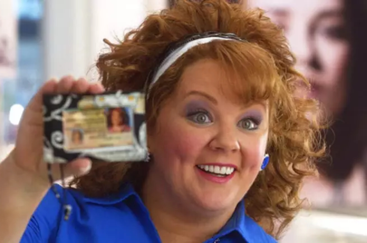 Woman holding up a wallet with ID, excited expression, workplace background