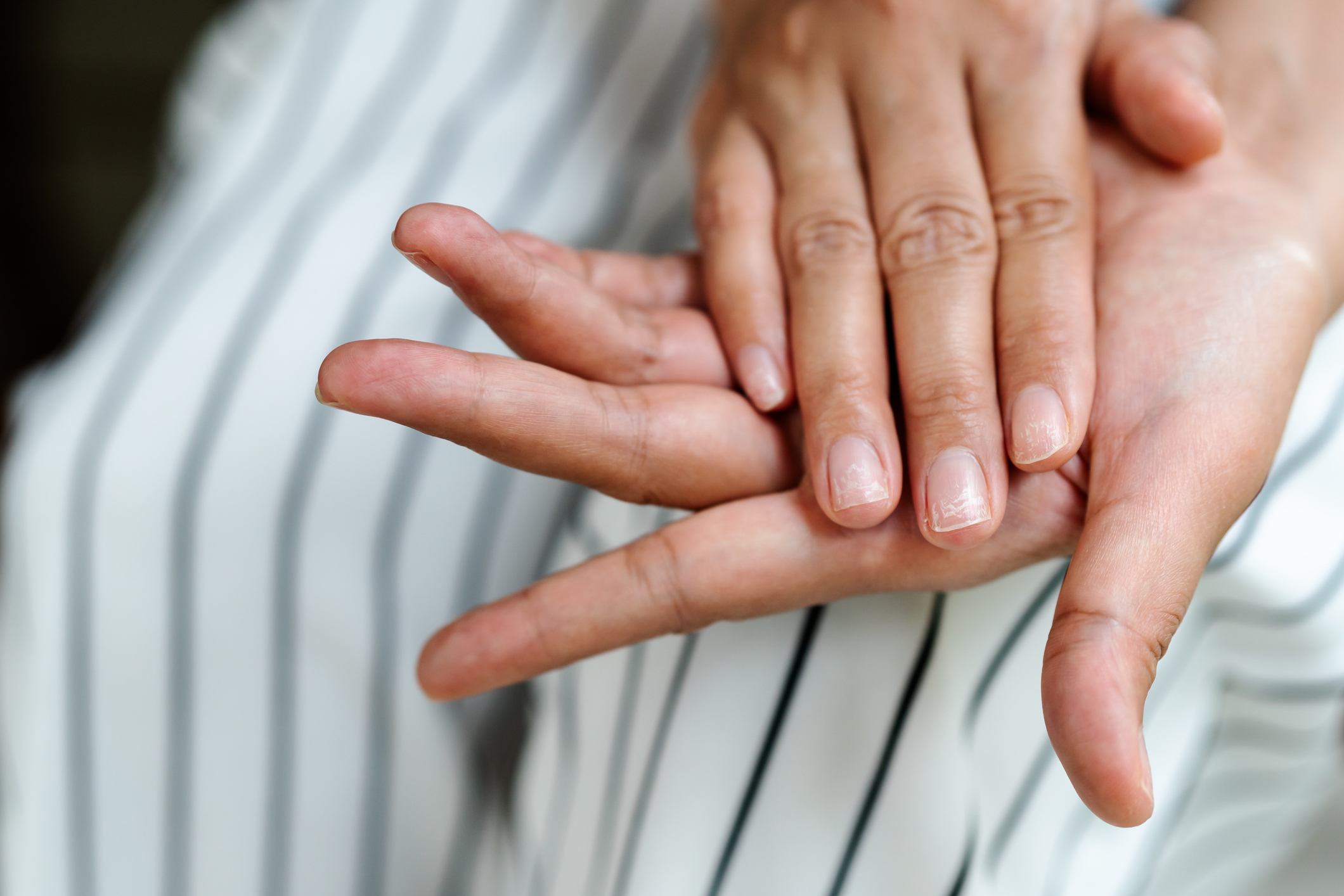 A close-up of a person gently placing their hand over another person's hand, both hands showing natural nails