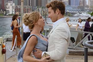 Two actors portraying characters in an outdoor scene with city background; both dressed in semi-formal attire