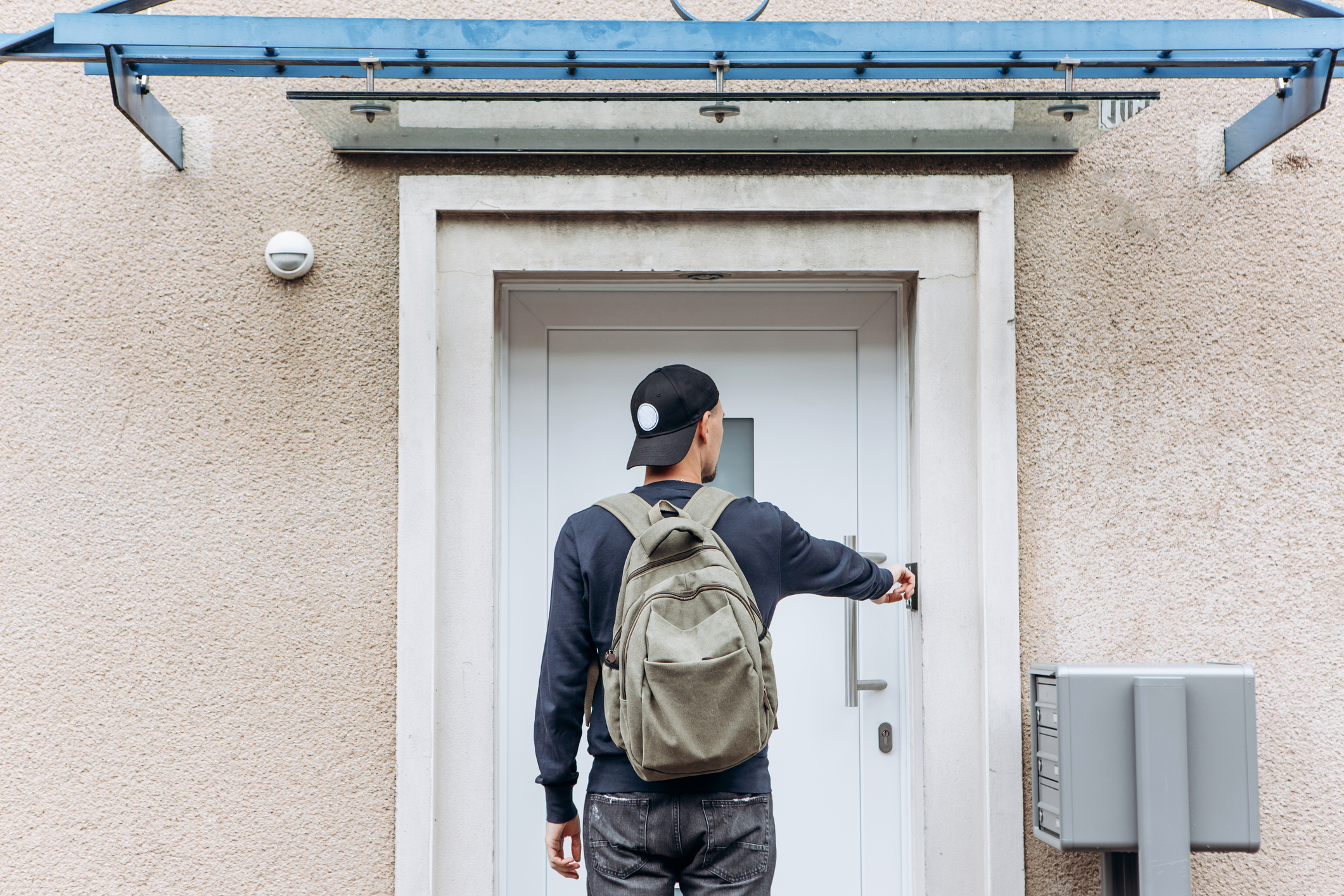 Person with backpack reaching towards a door handle under an awning