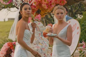 Alexandra Shipp and Hadley Robinson in wedding gowns stand near a floral arrangement at a wedding eating wedding cake as Claudia and Halle in Anyone but You