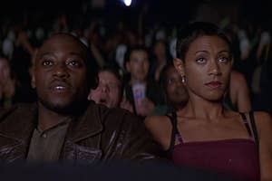 Omar Epps and Jada Pinkett Smith sit in a crowded movie theater, focusing intently on the screen ahead