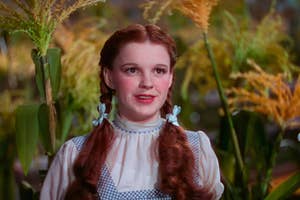 Judy Garland as Dorothy in "The Wizard of Oz," wearing braids and a gingham dress with a white blouse, with vegetation in the background