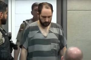 A man, flanked by law enforcement officers, appears in court wearing a striped prison uniform
