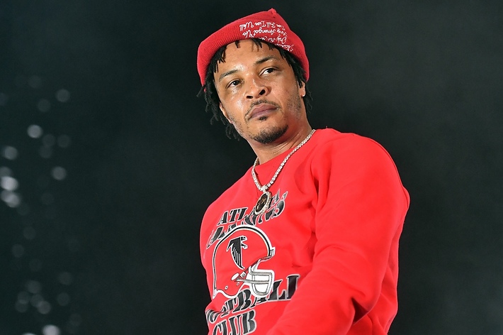 T.I. wearing a red hat with white text and a red sweatshirt with "Atlanta Football Club" logo and text, standing in front of a dark background