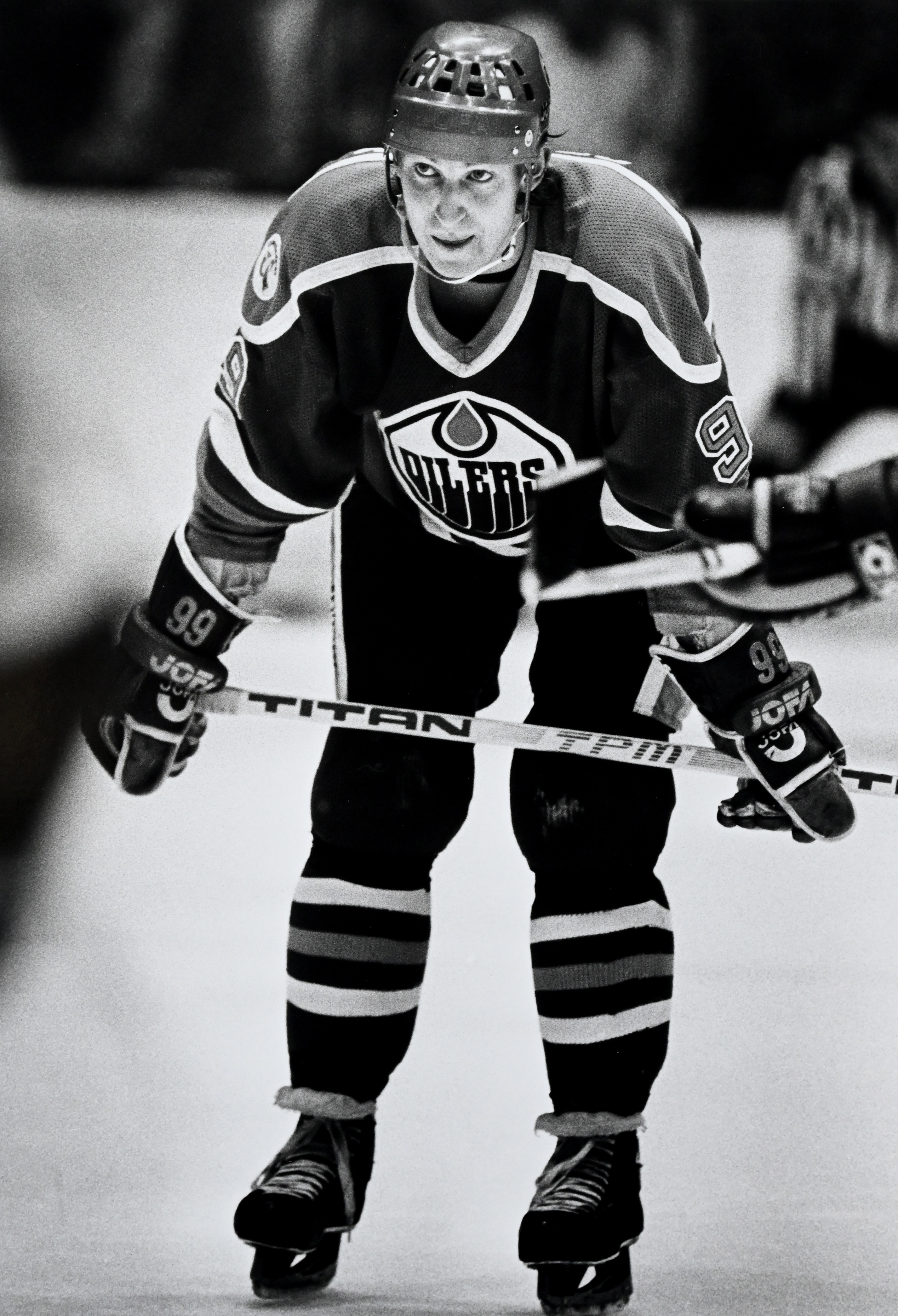 Wayne Gretzky in full hockey gear, wearing an Oilers jersey, stands on the ice during a game