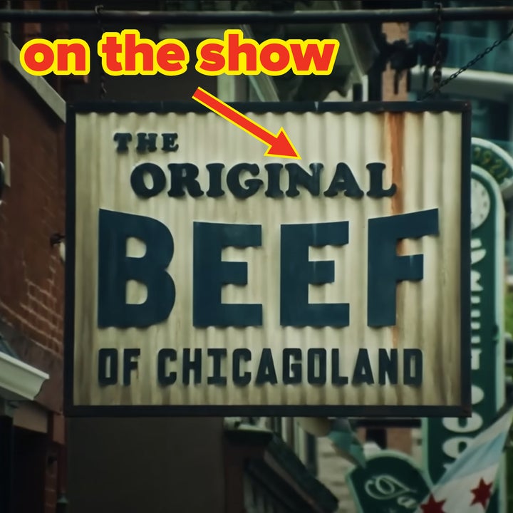 Sign reading "The Original Beef of Chicagoland" hangs outside a building on a street with other signs and greenery