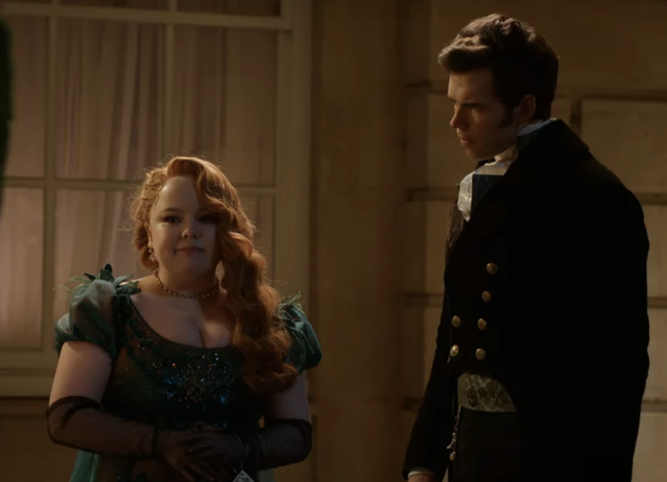 Nicola Coughlan y Luke Newton en una escena de época, ella lleva un vestido elegante y él un traje formal del siglo XIX