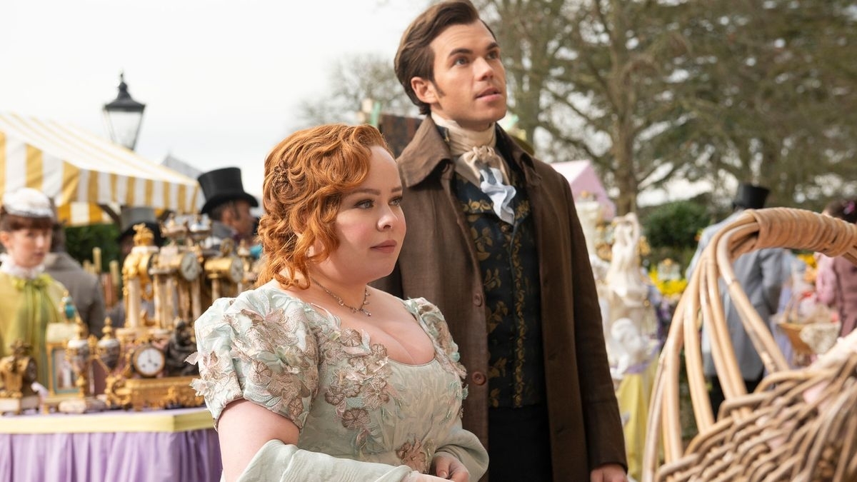Nicola Coughlan y Luke Newton en una escena de época de Bridgerton, rodeados de decoraciones victorianas y personas en trajes antiguos