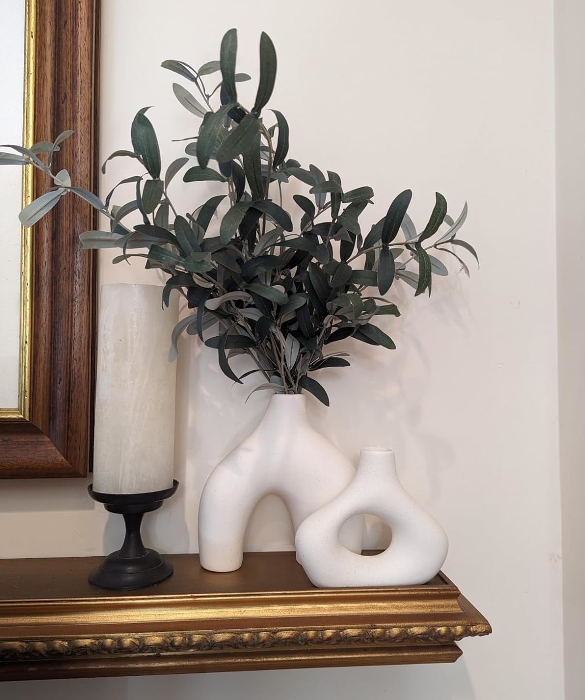 Artificial plant in a white torso-shaped vase next to a candle on a shelf. Unique home decor